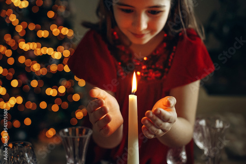 atmospheric, christmas photo, candle burning, children's hands nearby, girl's hands, christmas lights, garland in the background	
