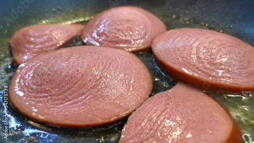 Boiled dairy sausage is fried in a frying pan. Pieces of milk sausage are fried in oil close-up.