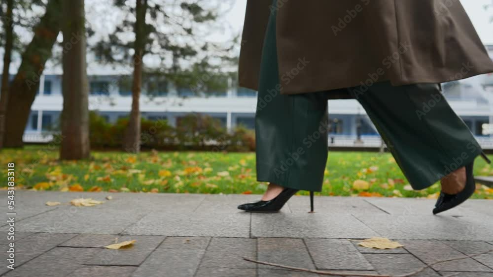 Unrecognizable Beautiful Legs Business Woman in High-Heeled Shoes and Wide Trousers Walk along Alley on Cloudy Autumnal Day. Stylish Businesswoman Walking in Autumn Park. Close-up, Slow Motion.