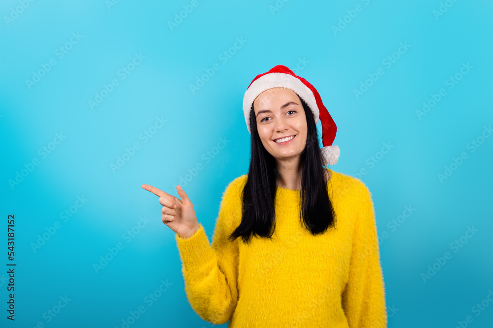 Photo of positive adorable female wearing Santa hat and yellow sweater promote recommend shopping season sales isolated on blue color background. Happy new year and Merry Christmas. Photo of positive adorable female wearing Santa hat and yellow sweater promote recommend shopping season sales isolated on blue color background. Happy new year and Merry Christmas.