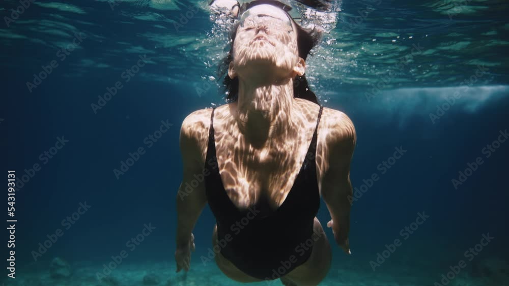 Slow motion close up shot of girl in swimming body suit swimming underwater air bubbles coming out of her nose