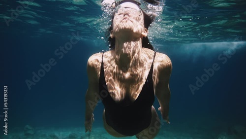 Slow motion close up shot of girl in swimming body suit swimming underwater air bubbles coming out of her nose