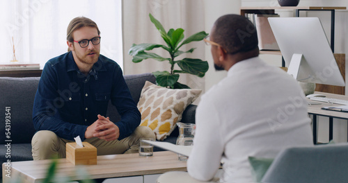 Man, patient or talking to psychologist on sofa in mental health, depression or anxiety counselling therapy. Psychology, stress or wellness counseling therapy help for person in rehabilitation clinic