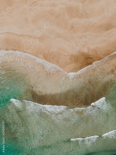 Vertical aerial view of sea waves coming onto a sandy shore