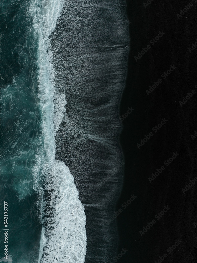 Fototapeta premium Vertical aerial top view of dark sea waves coming onto the shore