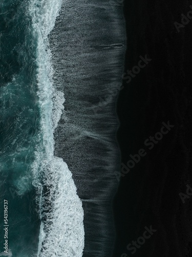 Vertical aerial top view of dark sea waves coming onto the shore