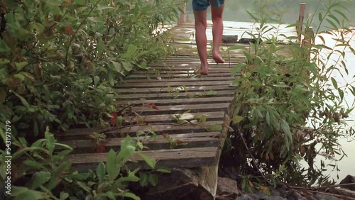 slow motion of a boy running on a wooden pier and jumping into the lake. High quality FullHD footage