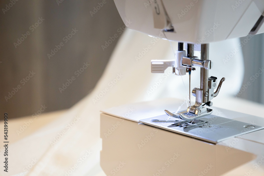 Close up side view of professional manufacturing machine at workplace. Needle pressure foot on a sewing machine with blurred white background. Apparel clothing production. Selective focus copy space.