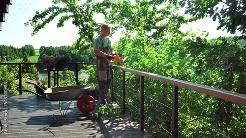 The gardener cuts the extra branches directly from the terrace in the garden with an electric trimmer. High quality 4k footage