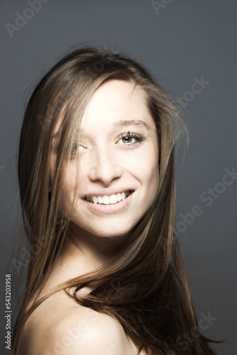 brunette girl turning head with flowing hair in the air studio portrait against gray background..