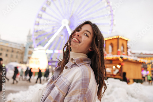 Positive young caucasian model looking into distance stands outdoor before winter holiday. Brunette wears turtleneck and shitr. Festive mood, weekends concept. photo