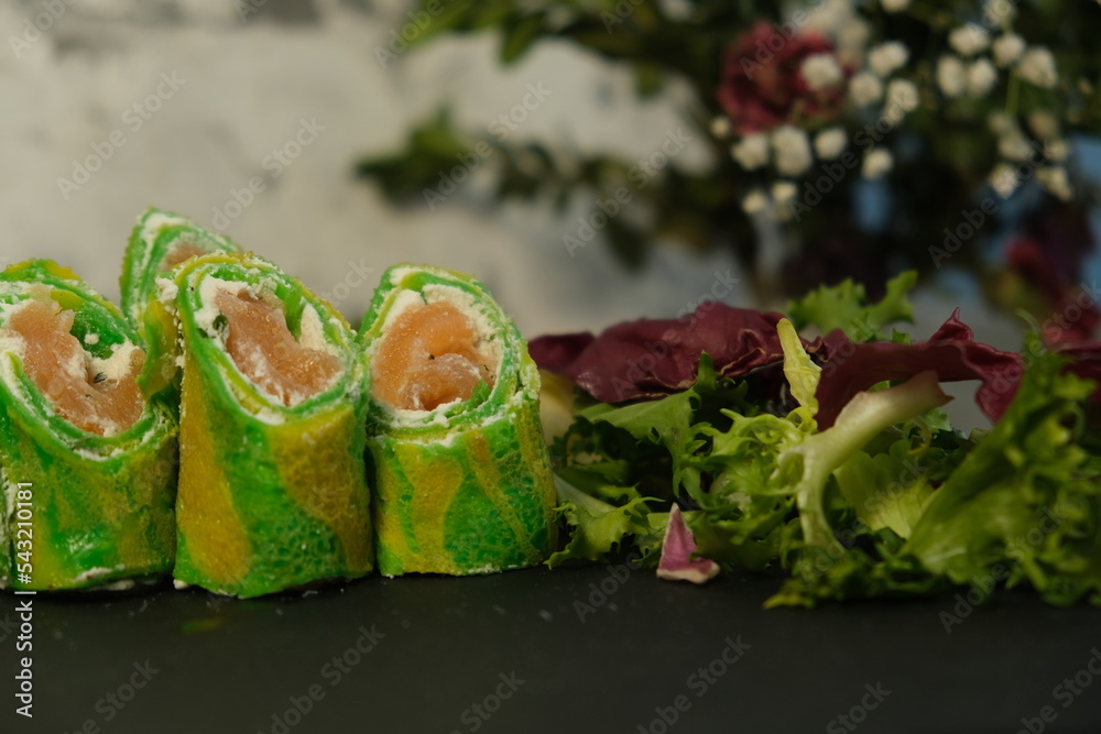 Green pancakes, 
New Year's bright snack, folded dough rolls, serving pancakes for Shrovetide. Filled with salmon and tender cheese. Zebra dough. Unusual serving food. Cooking, delicious food