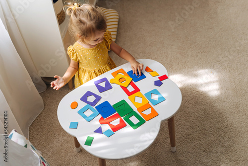 Obraz na plátně A little girl playing with wooden shape sorter toy on the table in playroom