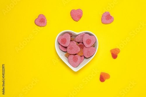 Top view of heart-shaped candies in a white heart-shaped bowl isolated on the yellow backrgound