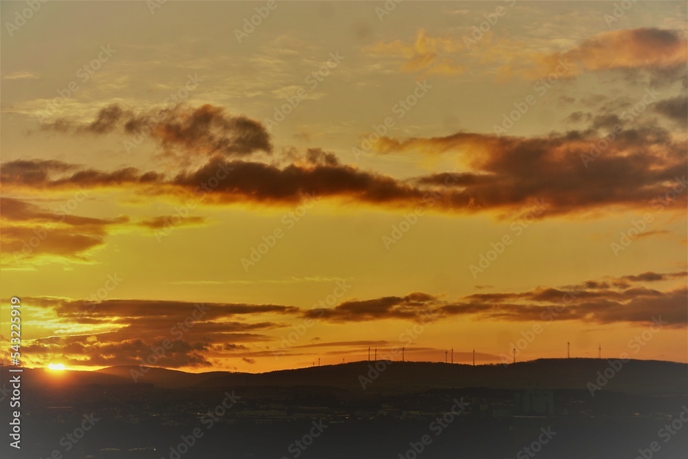 Grüne Berghügellandschaft mit Windrädern vor goldgelbem Himmel bei Sonnenaufgang am frühen Morgen im Herbst