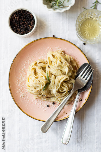 Creamy vegetarian tagliatelle Pasta with truffles and Parmigiano grated cheese served on a table with white linen, fresh rosemary, pepper, and white wine, top view close up