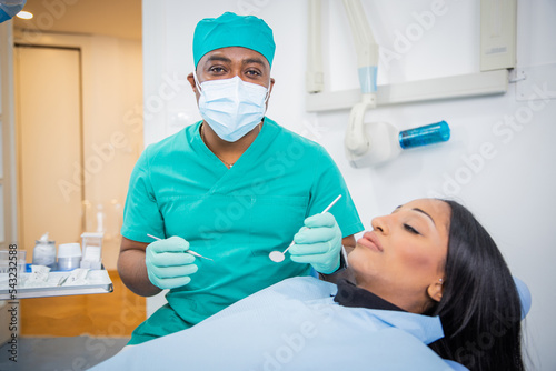An African dentist is holding working tools in the dental office with his patient sitting