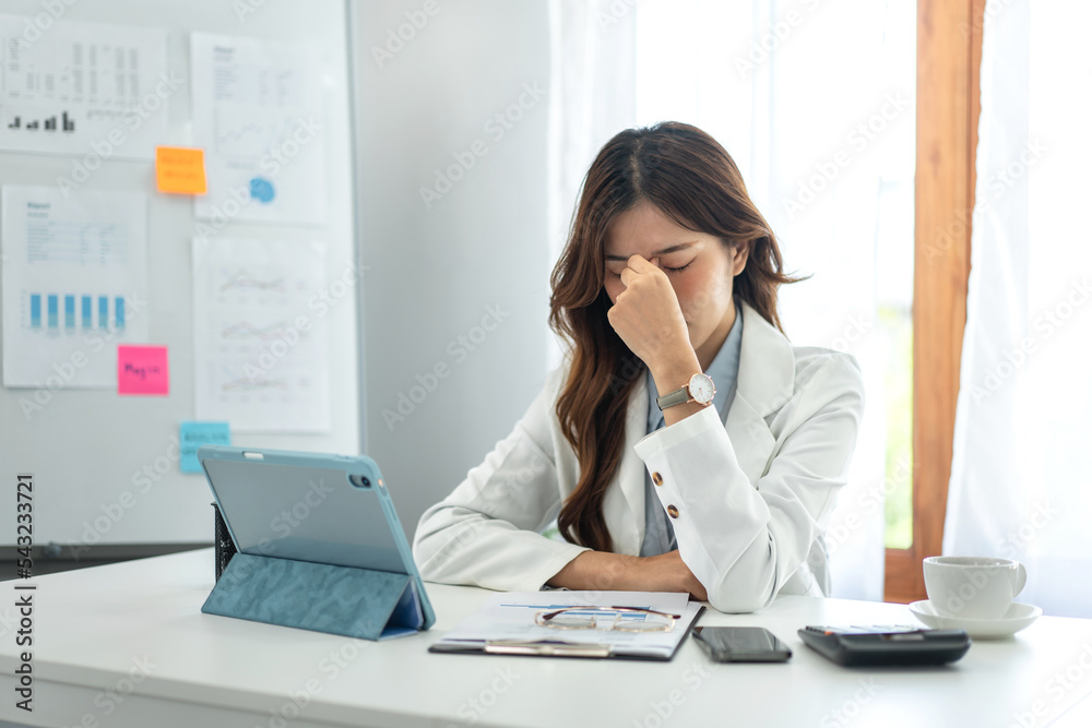 Businesswoman in suit stressful and suffering headache while working on tablet to thinking and analysis
