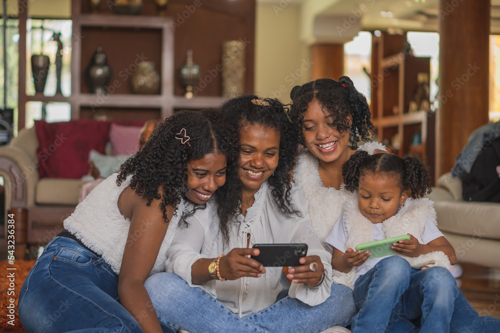 Glad Indian mother with daughters browsing smartphone in living room Glad Indian mother with daughters browsing smartphone in living room