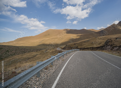 Asphalt highway in the mountains in autumn against the background of hills with grass and blue sky, autumn day in the mountains