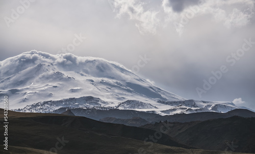 Panoramic view of the slopes of Mount Elbrus with glaciers and snowy cliffs and protruding rocks, in cloudy cloudy weather in the mountains
