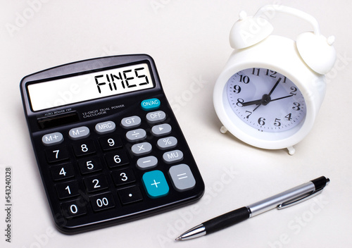 On the light table there is a black calculator with the text FINES on the scoreboard, a pen and a white alarm clock. Business concept