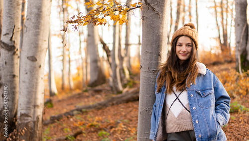 portrait of a girl in the autumn forest, Hello november, hello autumn.  Beautiful young woman enjoying autumn, posing next to tree, with the fallen leafs at the background. Wearing cozy blue jacket an