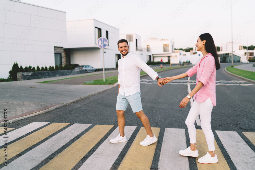 Happy diverse couple holding hands and walking on zebra crossing in street