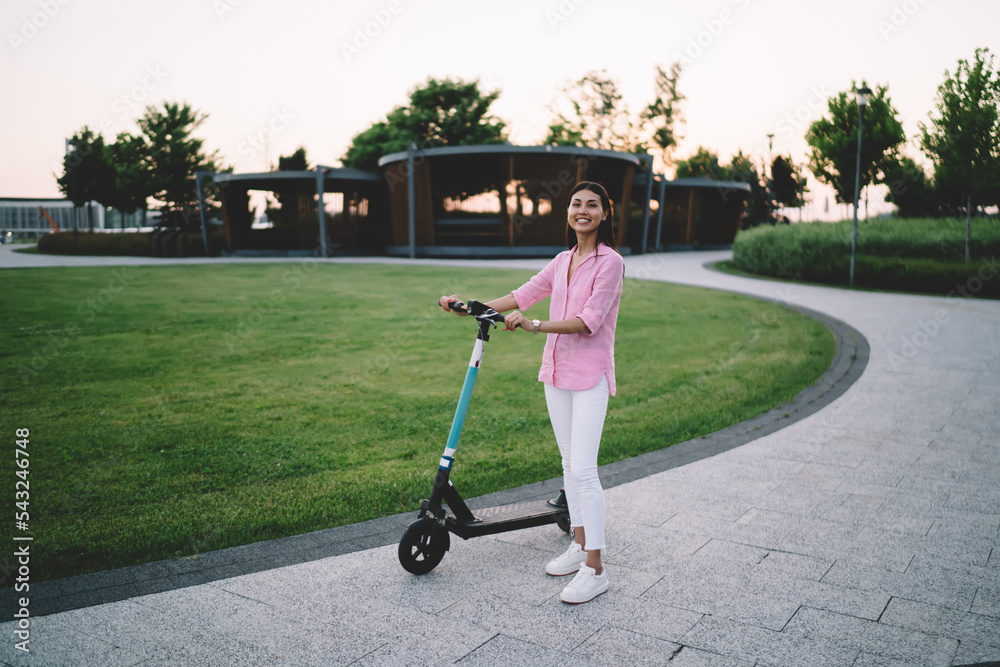 Smiling Asian woman with kick riding scooter standing and looking at camera Smiling Asian woman with kick riding scooter standing and looking at camera