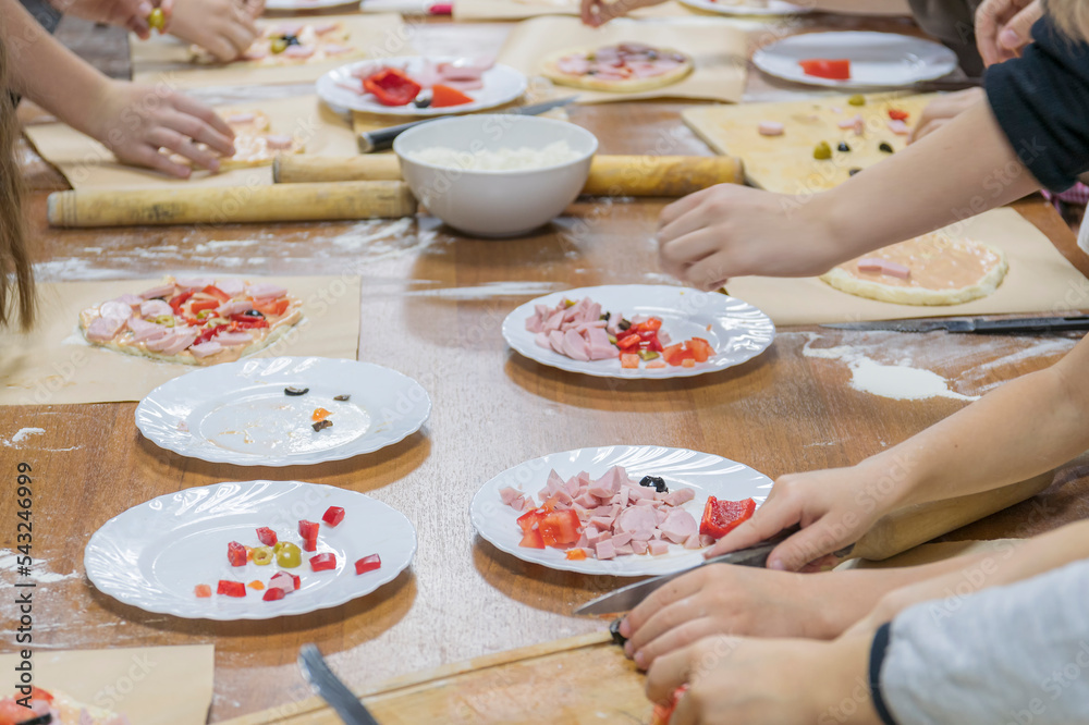 Children's hands are cutting food for making their first pizza on wooden table. Cooking master class Children's hands are cutting food for making their first pizza on wooden table. Cooking master class