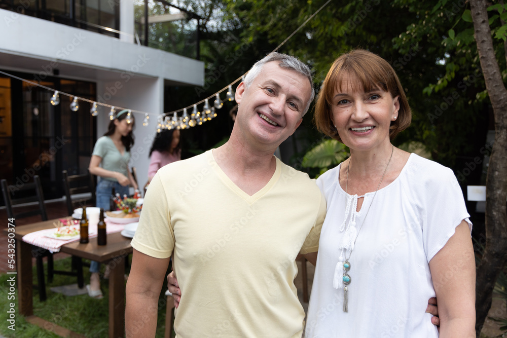 Naklejka premium Happy senior caucasian couple smile while there is an outdoor party behind them with a table of food
