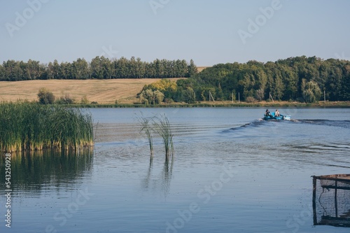 Two fyshemen in motor boat sails dissecting waves on river again