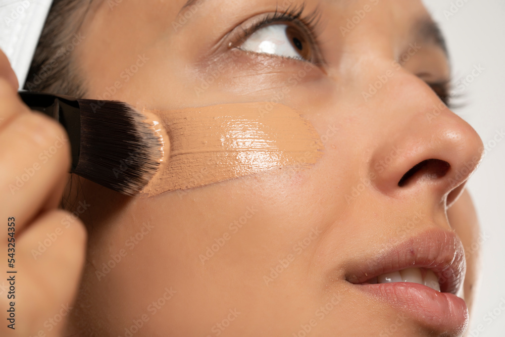 Φωτογραφία Young etnic woman applyes liquid founation on her face with makeup brush on whit