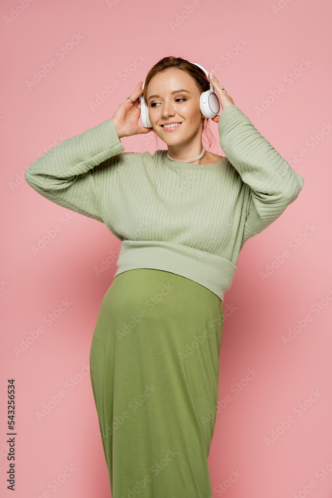 Happy pregnant woman in headphones looking away while listening music on pink background. Happy pregnant woman in headphones looking away while listening music on pink background.