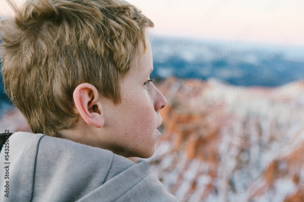 Blond hair boy overlooks snowy canyon in mountains Blond hair boy overlooks snowy canyon in mountains