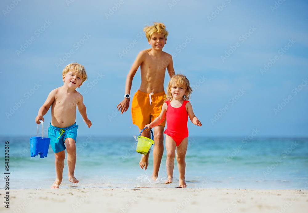 Three happy kids walk on the sand beach plying with toy buckets Three happy kids walk on the sand beach plying with toy buckets