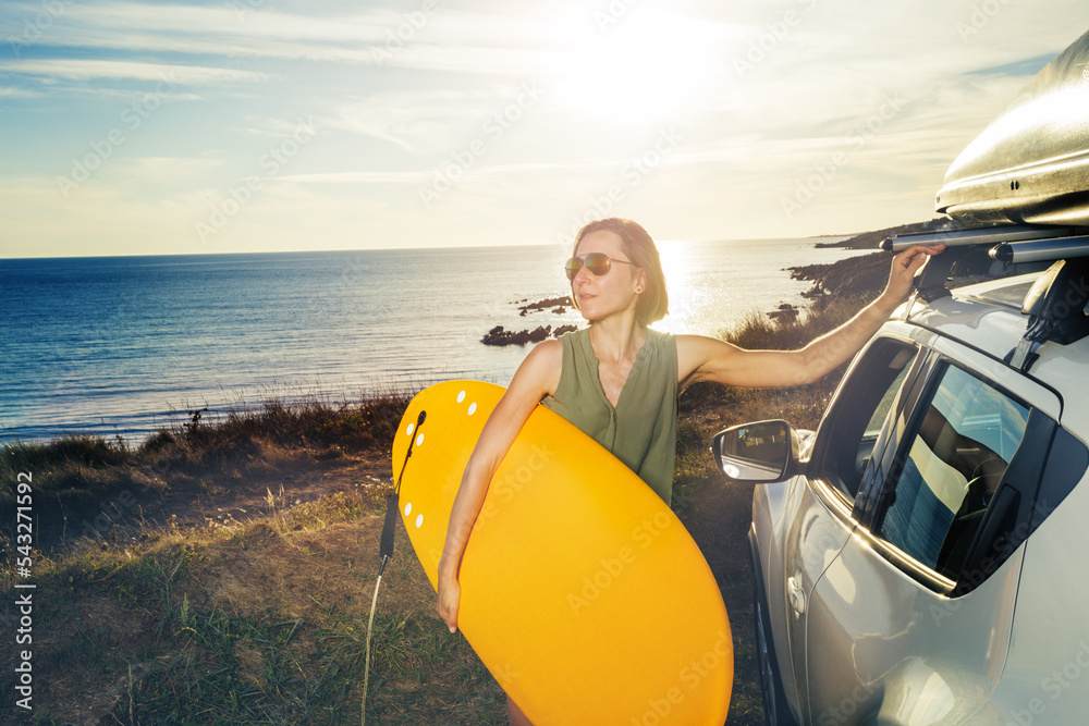 Woman on the cliff stand with surfboard over ocean sunset