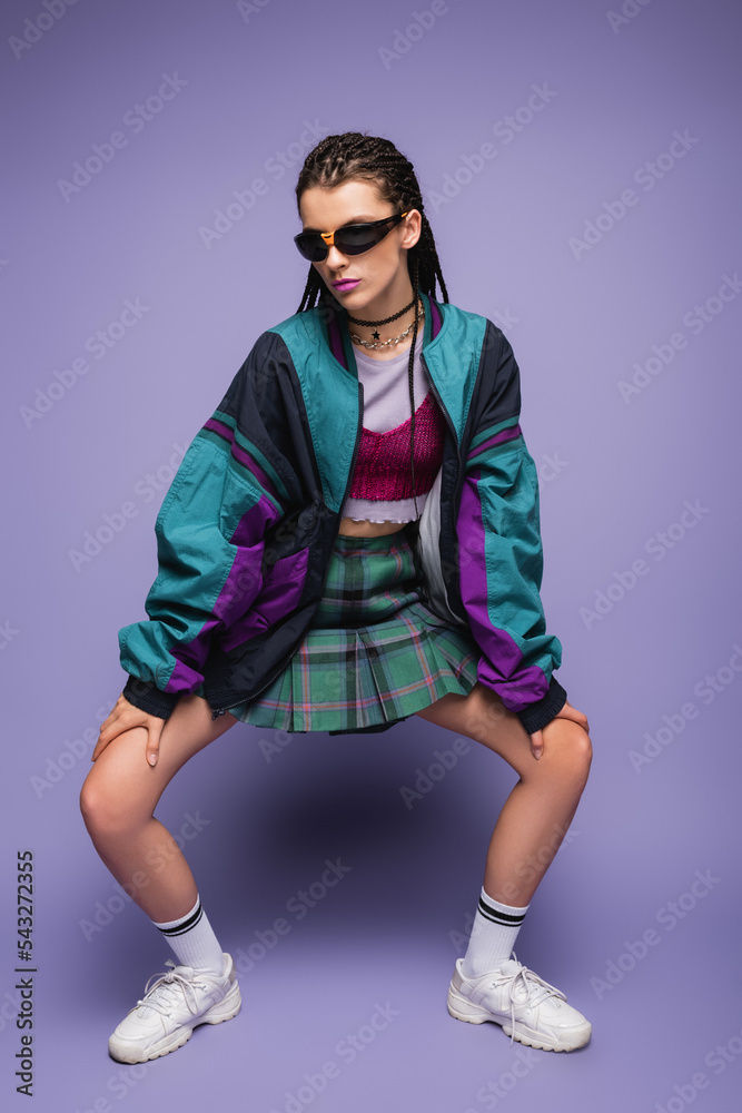 woman in sunglasses and nineties style clothes posing on purple background. woman in sunglasses and nineties style clothes posing on purple background.