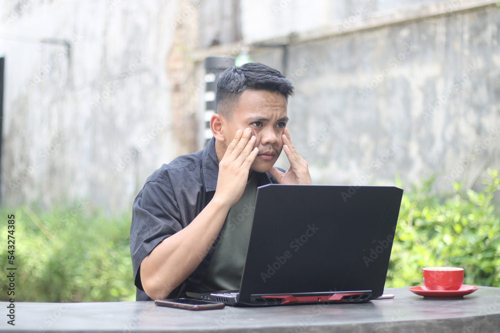 Attractive young Asian man using laptop confused in co-working space with unhappy face Attractive young Asian man using laptop confused in co-working space with unhappy face