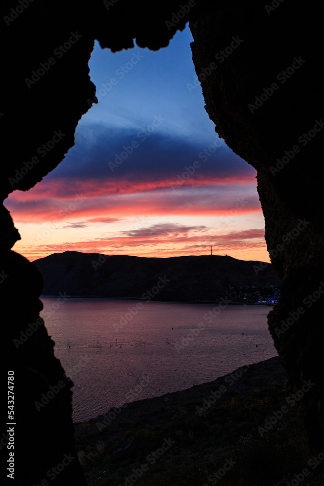 Orange sunset on the black sea against the backdrop of mountains and rocks. Vertical orientation.