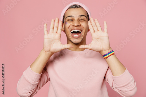 Young promoter gay man wear sweatshirt hat scream hot news about sales discount with hand near mouth isolated on plain pastel light pink color background studio portrait Lifestyle lgbtq pride concept