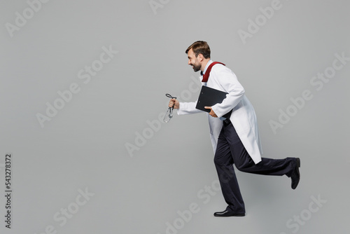 Full body side view male doctor man wears white medical gown suit work in hospital hold clipboard with paper documents run isolated on plain grey color background studio Healthcare medicine concept.