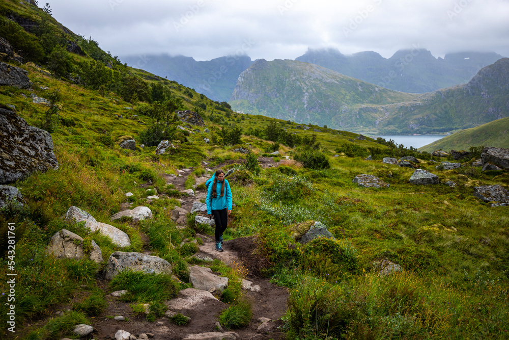 girl with a backpack hiking to the famous kvalvika beach on lofoten islands, norway; hiking in the norwegian fjords, rugged landscape of northern norway