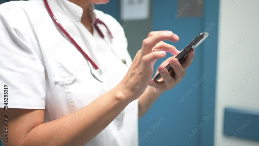 Cheerful pediatrician using smartphone in hospital hallway