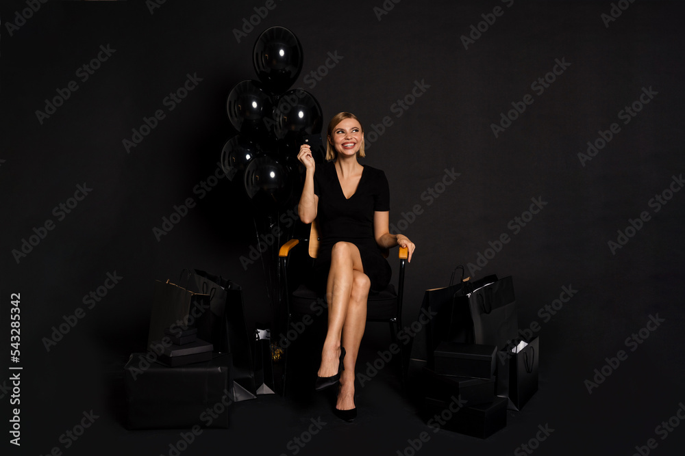 Woman holding credit card sitting with balloons and shopping bags isolated over black background