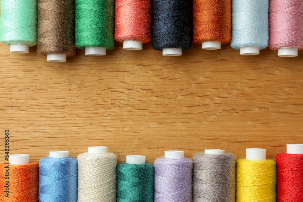 Many colorful sewing threads on wooden table, flat lay. Space for text Many colorful sewing threads on wooden table, flat lay. Space for text