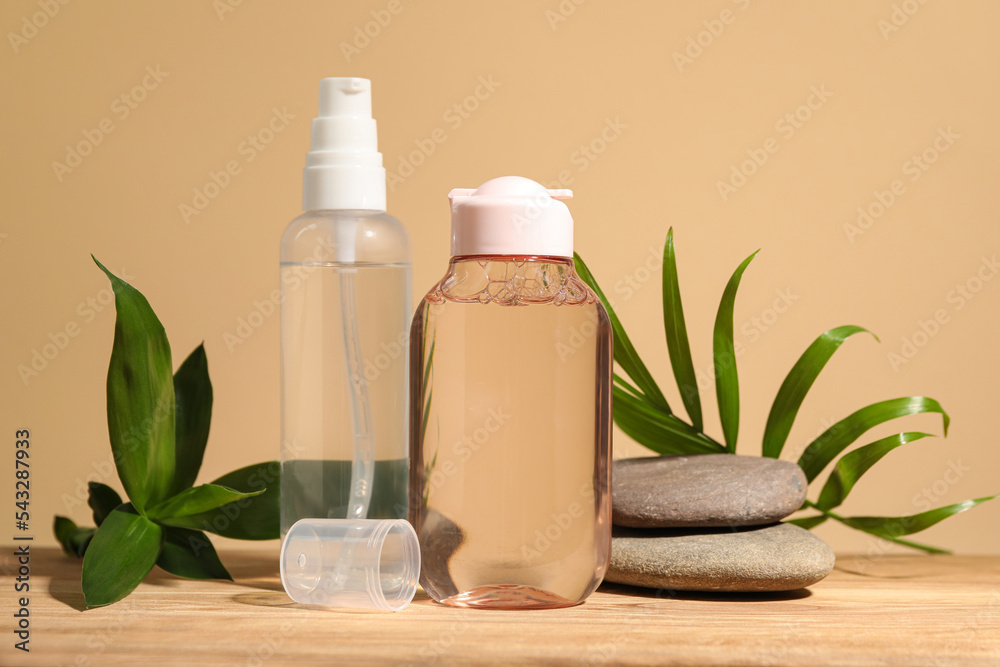 Bottles of micellar water, green leaves and spa stones on wooden table against beige background