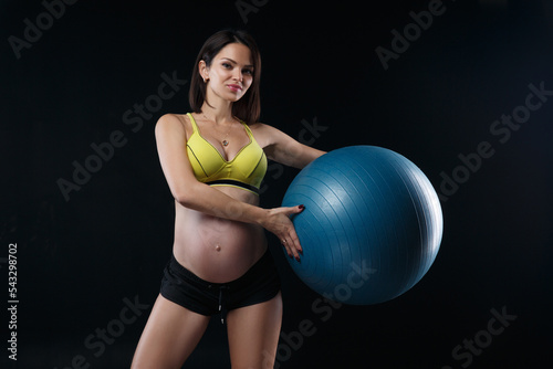 Athletic pregnant woman goes in for sports with ball isolated on a black background.