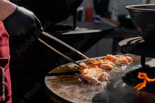 Chef cooking fried chicken meat pieces on brazier with hot flame at summer food market - close up. Outdoor cooking, barbecue, gastronomy, cookery and street food concept