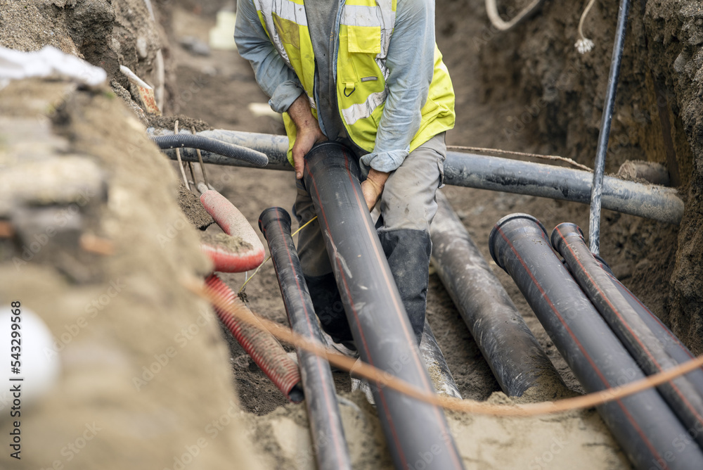 Stockfoto med beskrivningen Workers install underground pipes for water,  sewerage, electricity and fiber optics for the population of an urban  center. | Adobe Stock